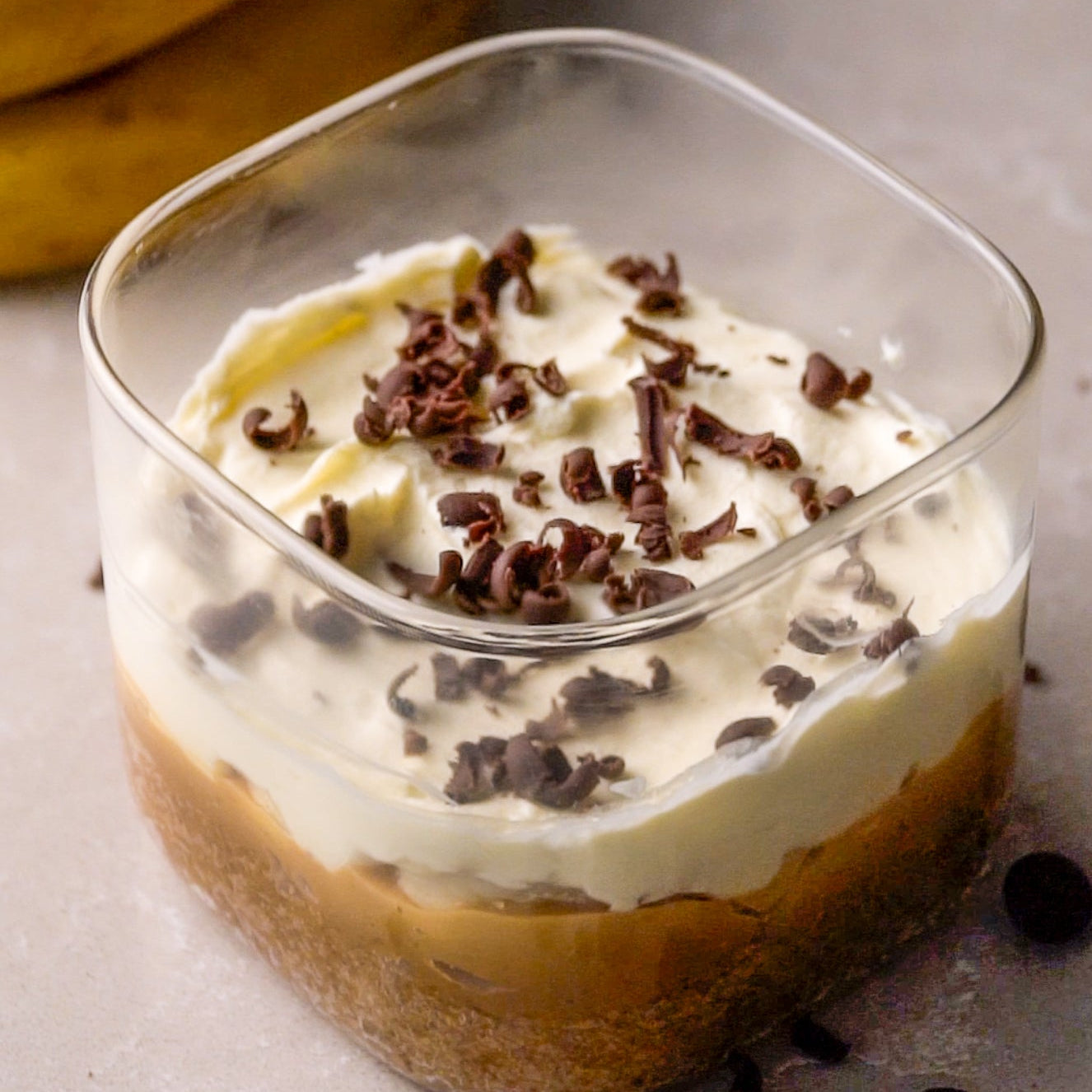 A serving of banoffee pie in a plastic container, topped with whipped cream and chocolate shavings.  Best Banoffee Pie in Singaopre
