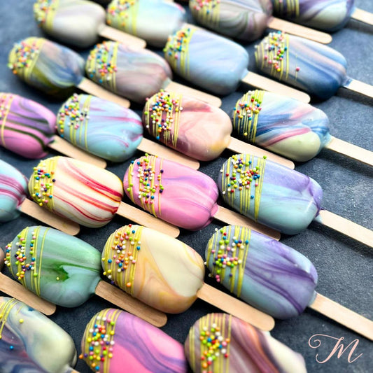 A selection of colorful eggless cakesicles with marbled designs and sprinkles on sticks.