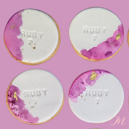 A collection of six watercolour biscuits with fondant coverage and gold leaf embellishments. Each biscuit has a different amount of gold leaf and watercolour detail, with a name embossed on them.